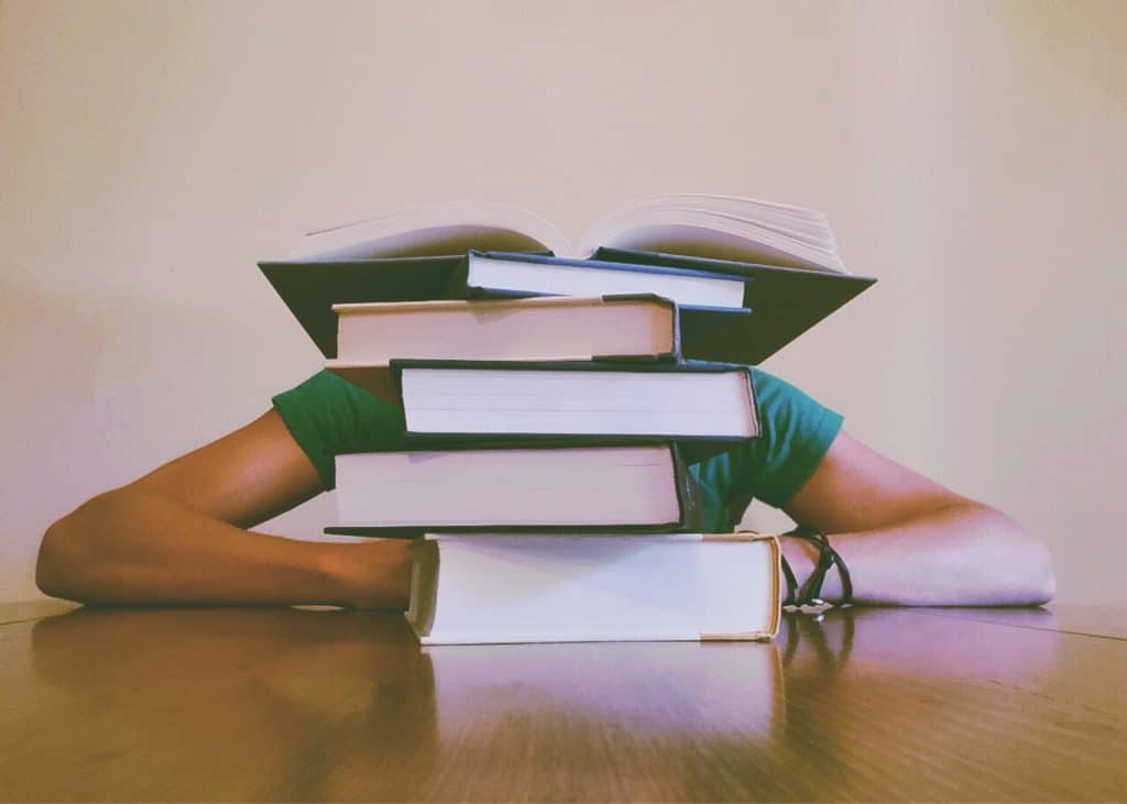 Eine Person sitzt am Tisch vor einem Bücherstapel und lässt den Kopf hängen - Symbolbild für Stress in der Klausurenphase.