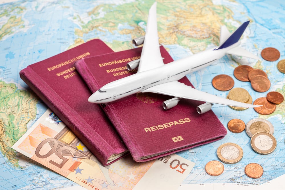 Auf einer Weltkarte liegen Reisepässe, Geld sowie ein kleines Miniaturflugzeug.
